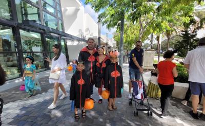 A family of trick or treaters pose on Miracle Mile in the shade on a sunny day